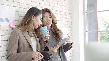 Two young Asian businesswoman college students or coworkers drinking coffee and talking in office. video