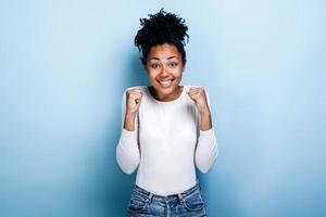 Overjoyed african American millennial girl isolated on blue studio background triumph get good news. Winner concept photo