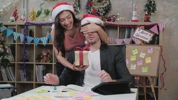Surprise two coworkers team and boss by giving gifts while business working before company holiday in office workplace, is decorated for the Christmas festival celebration and the new year party. video