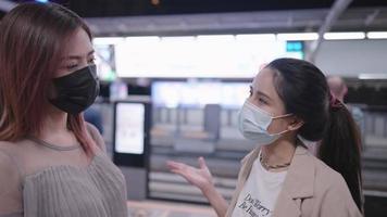 Two young adult asian women wear protective facemask talking to each other on the skytrain platform while que up waiting for the train, new normal life after pandemic, people adapt to new lifestyle video