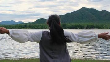 mujer asiática disfrutando de la vista de la naturaleza junto al lago al atardecer. estilo de vida y concepto de viaje de vacaciones video