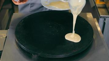 cuire des crêpes sur une plaque métallique chaude. restauration de rue et restauration rapide. le cuisinier verse le mélange de crêpes dans la poêle. video
