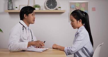 Portrait of young Asian doctor and patient sitting and discussing health examination results in clinic office. Charming male doctor giving advice to a female patient. Medical and health care concept. video