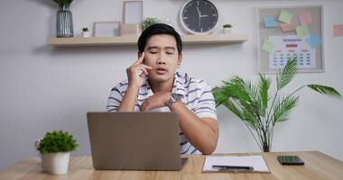 Porträt eines müden asiatischen Geschäftsmannes sitzt mit Laptop am Tisch. massiert die Schläfen und dehnt den Nacken. konzentriert sich auf die Arbeit, konzentriert sich auf den Monitor und sieht nicht blinzeln. video