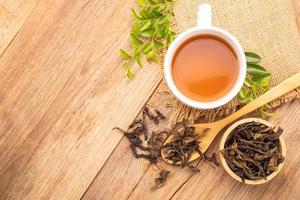 White cup of hot tea and dry tea leaf on wooden table photo