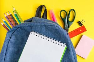 School backpack with office supplies on  yellow background. Place for text. photo