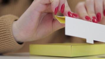 ett oigenkännlig kvinna veck en små gul kartong låda. produktion av kartong lådor från papper. förpackning tillverkning företag. närbild av händer håller på med papper hantverk på en kreativ lektion. video