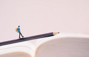 figuras de personas en miniatura con mochila caminando sobre lápiz y libro con espacio de copia, concepto de viaje y estudio en el extranjero foto