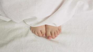 il bambino si sposta il suo gambe sotto il copertine. figli di mattina. risveglio. avvicinamento. video