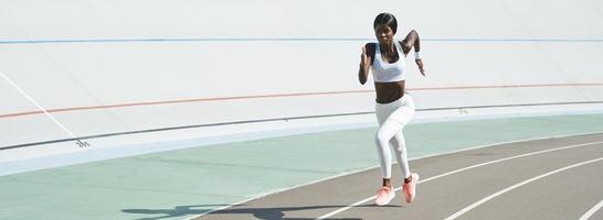 Beautiful young African woman in sports clothing running on track outdoors photo
