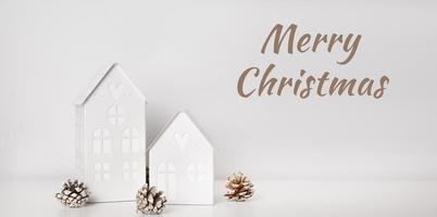 Merry christmas text with Winter decoration houses with lights near pine cones.Greetings card photo
