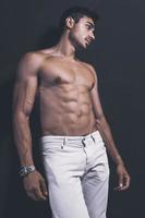 guapo modelo árabe masculino con cuerpo perfecto posando en el estudio. retrato de un modelo masculino atlético posando sobre fondo oscuro en el estudio. concepto de moda. foto
