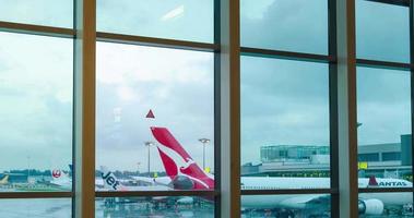 vista interior de lapso de tiempo dentro de la sala de la terminal de salida con ventana gigante con avión qantas airbus a330 y aviones de otras aerolíneas estacionados en el aeropuerto video