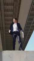 vidéo verticale, homme d'affaires avec une mallette d'affaires dans ses mains surmonte l'obstacle en retard pour une réunion importante. entrepreneur ou employé de bureau se précipitant pour travailler. homme en tenue de soirée sautant parkour video