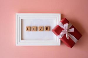 caja de regalo roja y marco de fotos con letras de amor sobre fondo rosa para regalar en vacaciones con espacio para copiar texto. vacaciones, presente, dando. día de año nuevo, día de navidad, año nuevo chino.