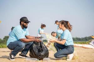 trabajar como voluntario, caridad, limpieza, personas y ecología concepto - grupo de contento voluntarios con basura pantalones limpieza zona en arenoso costa. foto