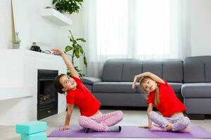 dos niñas practicando yoga, estiramientos, fitness por video en el cuaderno. entrenamiento de educación en línea distante, aeróbico en casa. estilo de vida saludable, coronavirus, quédate en casa. los niños hacen deporte en casa en cuarentena. foto