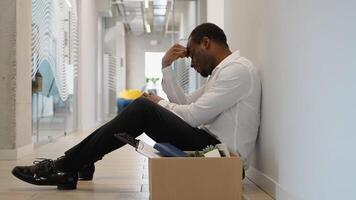 Sad fired worker sitting frustrated and upset in the hallway near office with dismissal box video