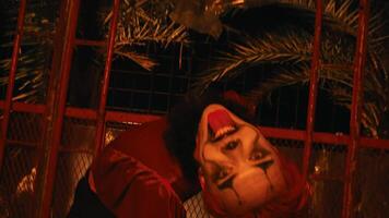 a creepy clown with red hair and costume poses and dances in a haunted hut that lights up red video