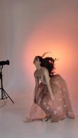 A young woman, a ballerina girl dancing, gently moving her arms and fingers on a pink background in a studio, slowmo, medium. Lady brown-haired woman with long hair video