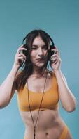 Beautiful girl enjoying music under the flashes. Pretty young woman dancing and listening music with black headphones. yellow underwear. blue background. vertical video for phone.