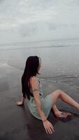 brunette girl lying on the sand and running from the wave, vertical video