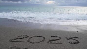 content Nouveau année 2025 main écrit chiffre 2025 lavé par vague sur le mer plage. abstrait Contexte de à venir Nouveau année 2025 et en quittant année de 2024. video