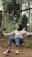 Pensive smiling young woman with headscarf resting in comfortable hammock at green garden. photo