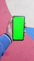 uma homem dentro a urbano configuração detém uma Smartphone com uma verde tela, exibindo moderno tecnologia video