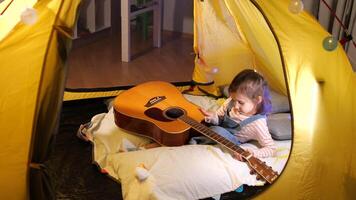 pequeno menina jogando música em guitarra dentro wigwam. passatempo do musical criança video