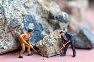 un miniatura trabajador trabajador perforación un grande rock . temas de perserverancia, fuerza y mano de obra. foto