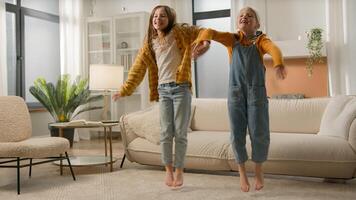 Two carefree Caucasian children little girls sisters laugh jumping floor celebrating moving bouncing kids friends daughters dancing music having fun together family home apartment friendship housing photo