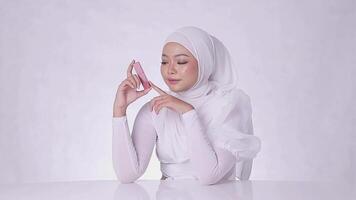 beauté maquillage lèvres adulte femme hijab magnifique de bonne humeur incliné Regardez à caméra main serrer incliné de côté rouge à lèvres récipient isolé blanc Contexte video