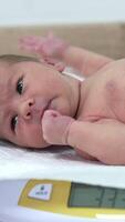 Naked child lying on the electronic scales and hiccupping. Cute Newborn baby being weighed in Maternity unit in the hospital. Vertical video