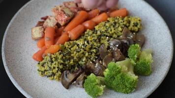 Colorful vegan vegetarian dish consists of tofu, broccoli, quinoa, mushrooms and carrots on a dark textured background video