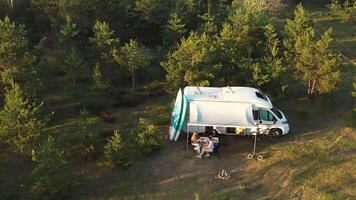 une famille de Trois séance à une table à l'extérieur une camping car dans le les bois . Voyage concept video
