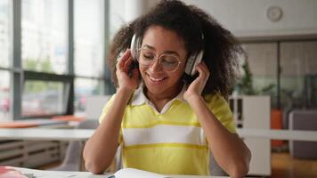 africano americano mujer estudiante niña hembra en lentes escuchando música audio canción sonido en auriculares auriculares trabajando aprendizaje estudiando descanso gratis teniendo divertido alegría sonriente adentro Universidad Universidad video