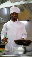 africano americano chefe de cozinha cozinhar derrama girassol ou Oliva óleo para dentro a frigideira. vertical video