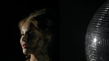 Close-up of beautiful thirty-year-old woman's face, wearing expensive jewelry, dancing in nightclub under light of disco ball. Slow motion video