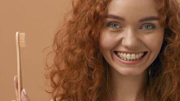 uma jovem mulher com encaracolado vermelho cabelo sorrisos brilhantemente enquanto segurando uma escova de dente. a caloroso fundo acrescenta uma acolhedor sentir, destacando dela alegre expressão e a importância do dental Cuidado. video