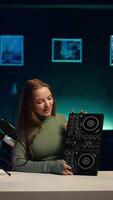 Vertical Cheerful girl mixing on DJ turntables, doing music production tutorial for online streaming channel. Smiling young content creator playing around with stereo sound mixer, camera B video