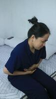 Young woman sits on bed suffering abdominal pain, menstrual period video