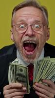 Excited mature man waving dollars. Happy funny elderly businessman showing banknotes on camera with opened mouth. Positive emotions. Vertical video