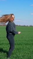 Happy girl in jeans on a green meadow. Beautiful young woman jumping joyfully on a field in a bright day. Cheerful model among nature. Vertical video