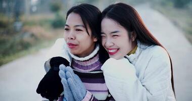 ordinateur de poche sélectif concentrer tir, deux asiatique femmes dans chaud Vêtements Heureusement supporter et parler dans le du froid Matin air. hiver vacances video