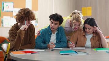 Four school Caucasian students pupils studying indoors male female prepare exams write homework teamwork learning men women girls guys teenagers writing discuss talking cooperation communicate friends video