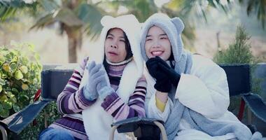 Two Asian women in warm clothing sit on chairs and chat happily while enjoying the cold morning view. Winter Holiday video