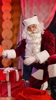 Christmas gifts. Santa Claus putting presents under the Christmas tree at New Year's eve.Santa with presents near at decorated Christmas tree near fireplace. Vertical video