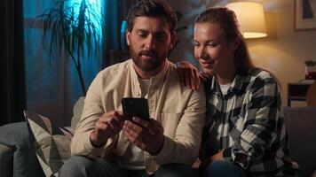 feliz família conectados compras às casa caucasiano amoroso casal mulher homem navegando Smartphone tarde final de semana sorridente menina cara Móvel telefone aplicativo banco crédito compra Internet comprando noite insônia video