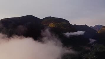 The drone flies high above the clouds that cover the tops of the Alps. Village in a lowland between mountains in twilight evening light. Austria video